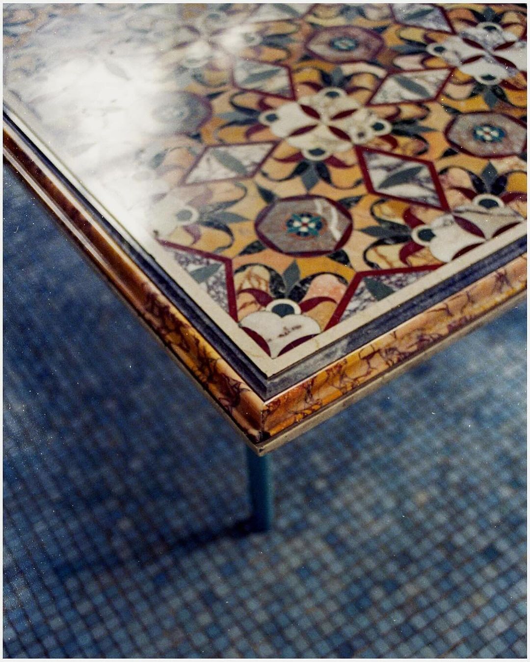 Elevated shot of a marble table with mosaic tile detail featuring floral and geometric patterns in various colors, set against a tiled floor.