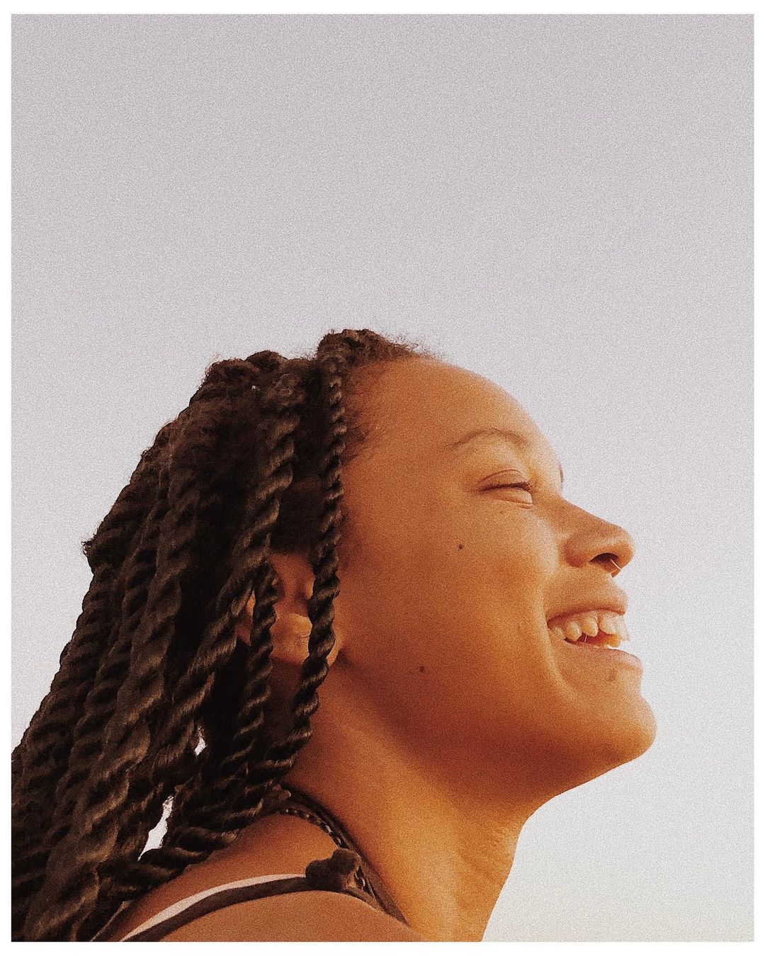 Profile portrait of a smiling Black woman with braided hair captured outdoors in Paris by Rodrigo Oliveira.
