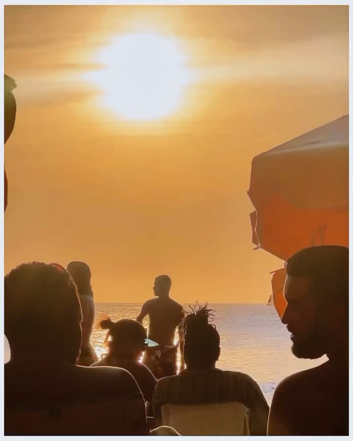 People on a beach during sunset, enjoying the view with orange sky and gentle waves creating a serene and relaxing atmosphere.