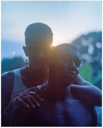 Two black men posing outdoors with warm sunlight flaring behind them in a portrait by photographer Rodrigo Oliveira.