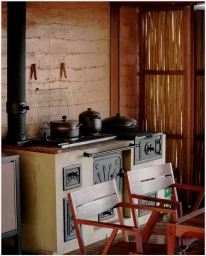 Traditional wood-burning stove with black pots and two wooden chairs against a textured wall