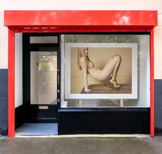 Framed fashion photograph in a shop window with a blonde model wearing nude clothing and gold painted limbs and platform shoes.