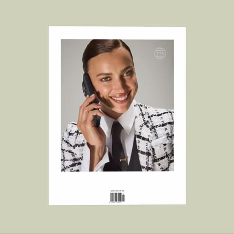 Fashionable woman in a suit jacket speaks on a smartphone, smiling in a studio shot with a clean background, demonstrating beauty and style.