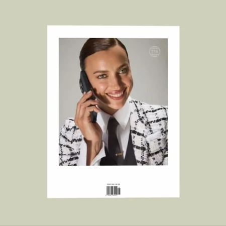 Fashionable woman in a suit jacket speaks on a smartphone, smiling in a studio shot with a clean background, demonstrating beauty and style.