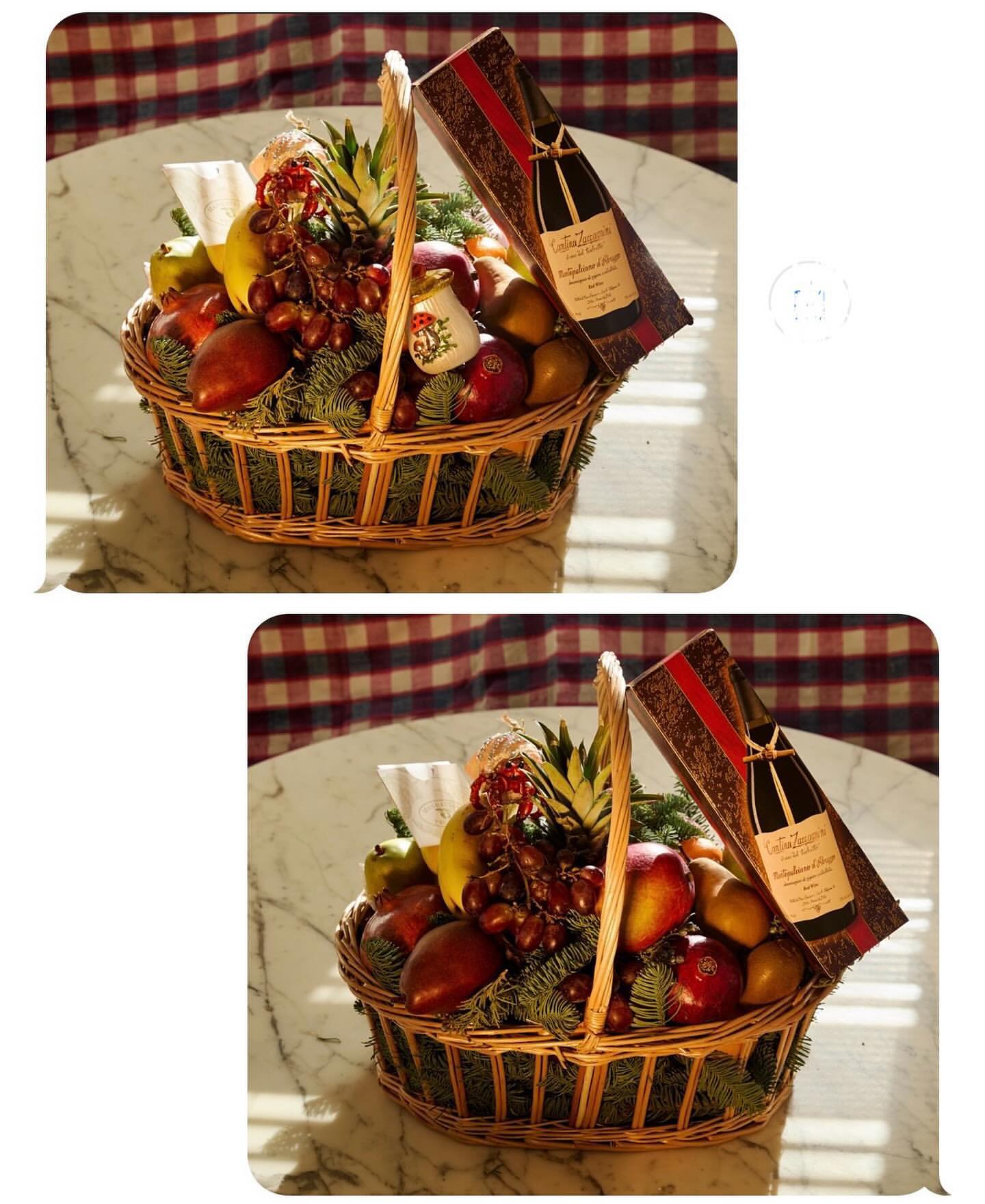 Fruit basket overflowing with apples, pears, grapes, and pineapple next to a decorative bottle on a marble table with a plaid tablecloth.