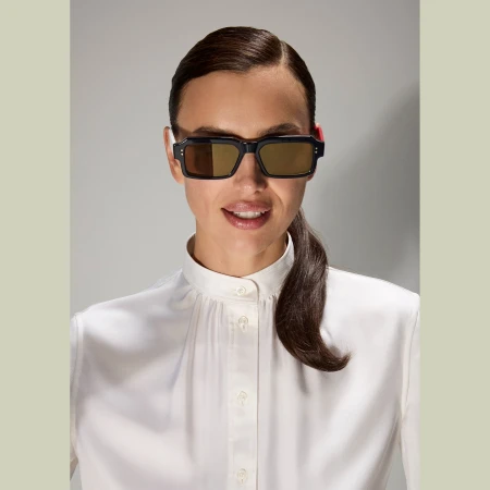 A woman in a white blouse and black sunglasses poses against a neutral background, showcasing fashion and beauty in a studio shot.