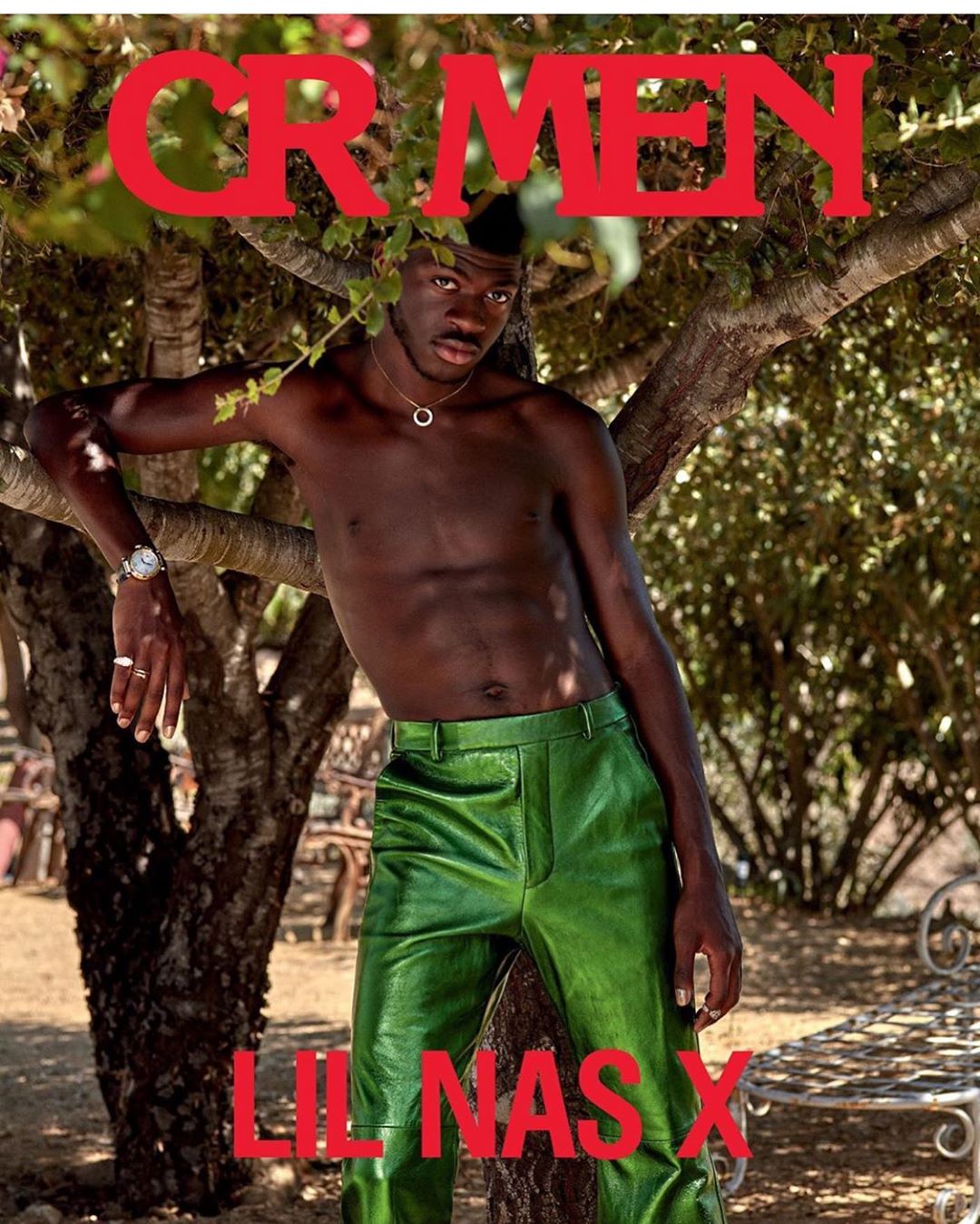 A striking magazine cover features a topless Lil Nas X in green leather pants, leaning against a tree, set against an outdoor backdrop.
