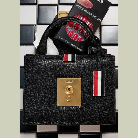 Black leather handbag with a gold clasp and nail tips on a black-and-white tiled surface, showcasing beauty and fashion accessories.