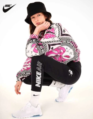 Model wearing a black bucket hat, patterned jacket, black leggings, and white sneakers crouching against a white background