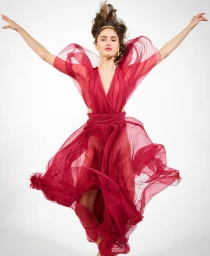 Model in a flowing red sheer gown posing dynamically with arms outstretched against a white background