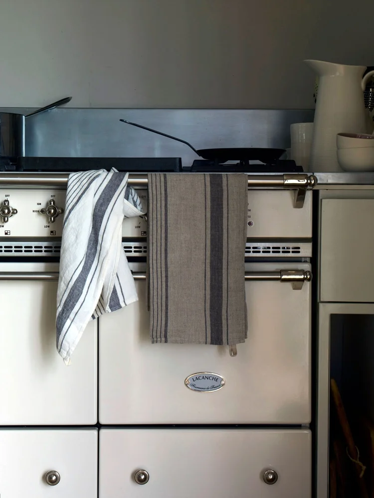 Kitchen interior featuring a white Lacanche range oven with striped towels, complemented by stainless steel and white kitchenware.