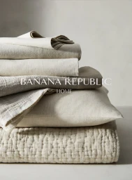 Stack of folded neutral linen bedding, textured pillow, and quilted blanket for Banana Republic Home.