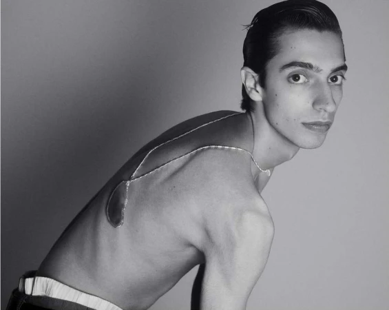 Monochrome portrait of a man wearing a metallic body jewelry piece draped across his bare back by Romain Duquesne