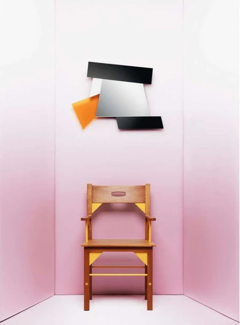 Minimalist interior set featuring a wooden chair with yellow accents placed beneath a modern abstract mirror against a pink wall backdrop.
