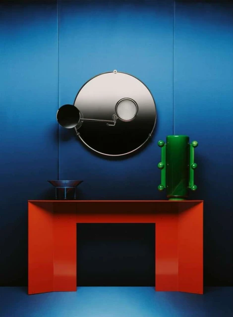 Modern interior design with a red console table, decorative mirror, and green vase against a gradient blue wall.