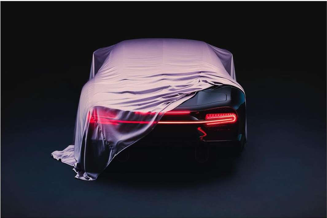 Rear view of a black sports car partially covered by a silver fabric sheet in a dark environment, showing sleek tail lights.