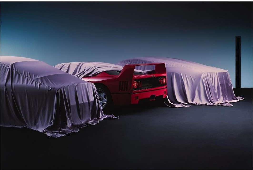 Red Ferrari F40 supercar partially unveiled with purple satin covers in a studio setting with a gradient blue background.
