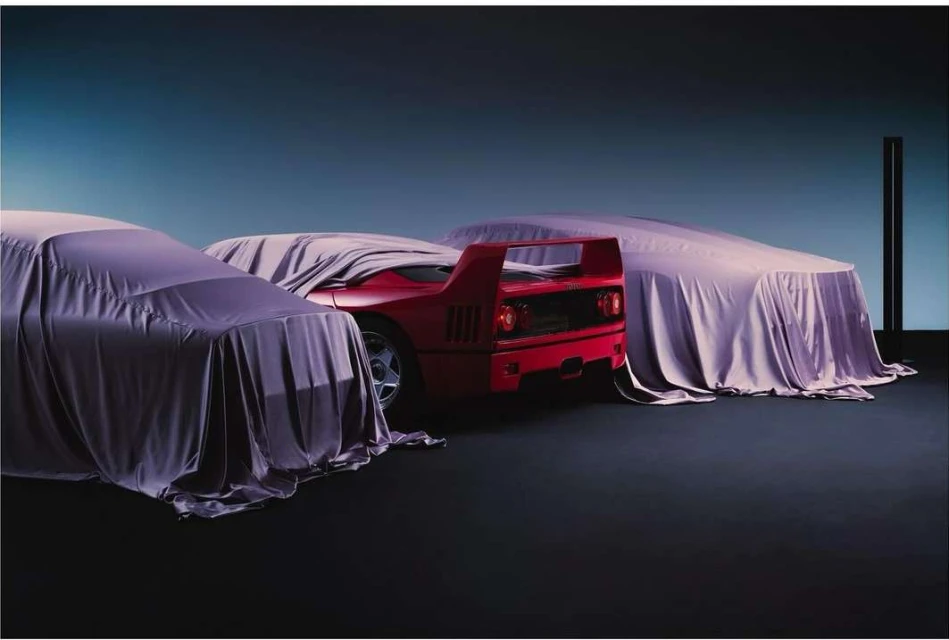 Red Ferrari F40 supercar partially unveiled with purple satin covers in a studio setting with a gradient blue background.