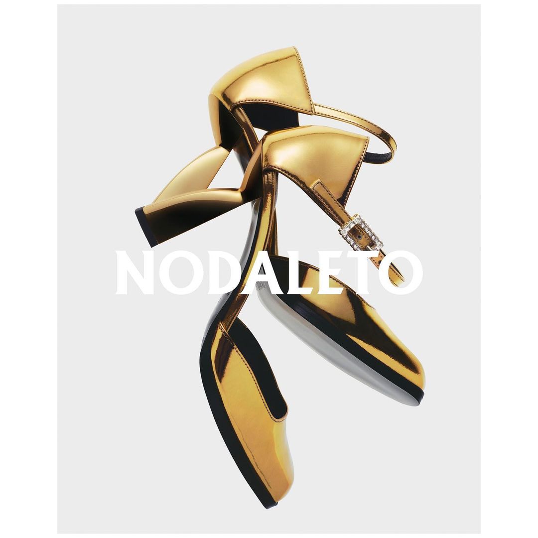 Pair of gold Nodaleto heeled sandals with ankle straps and square toes on a neutral background. Fashion footwear product shot.