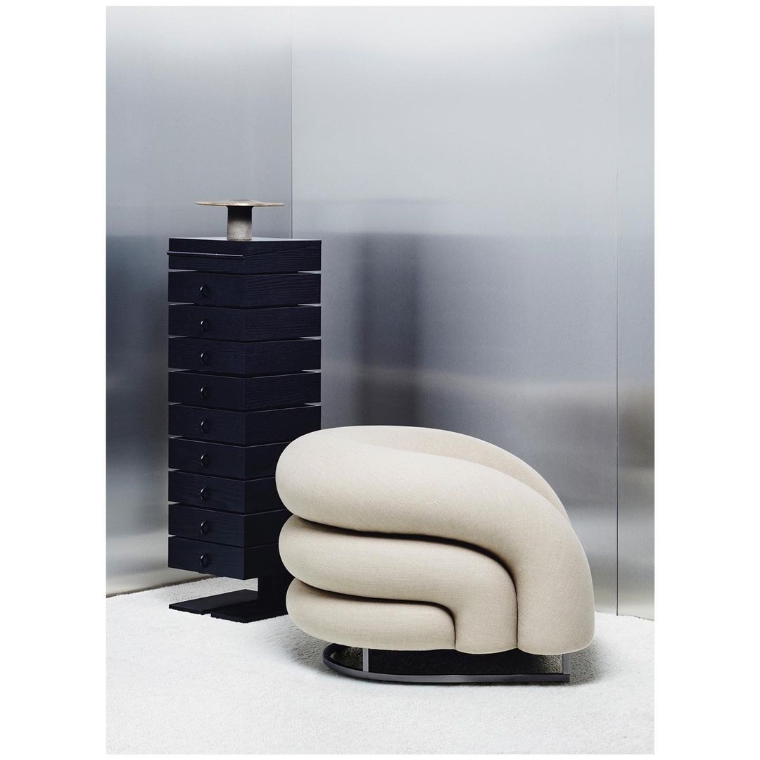 Modern interior featuring a unique rounded chair with a black cabinet against a gray backdrop and a white carpeted floor.