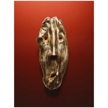 A metallic gold sculptural face mask mounted against a deep red gradient background photographed by Romain Roucoules in Paris.