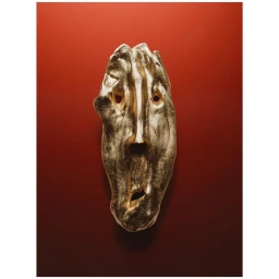 A metallic gold sculptural face mask mounted against a deep red gradient background photographed by Romain Roucoules in Paris.