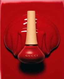 Close-up product shot of a red Gucci nail polish bottle resting on a glossy red pool background