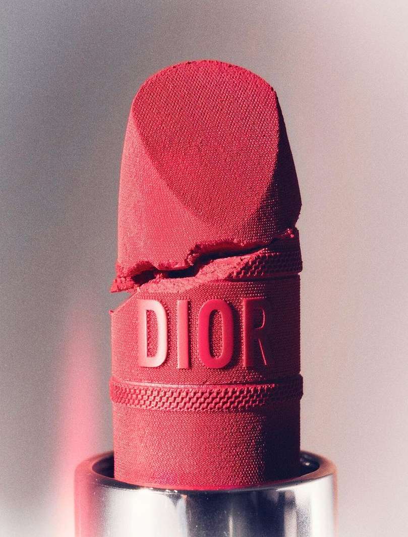 Macro shot of red Dior lipstick showing the product's texture and the embossed Dior logo, set against a gradient background.