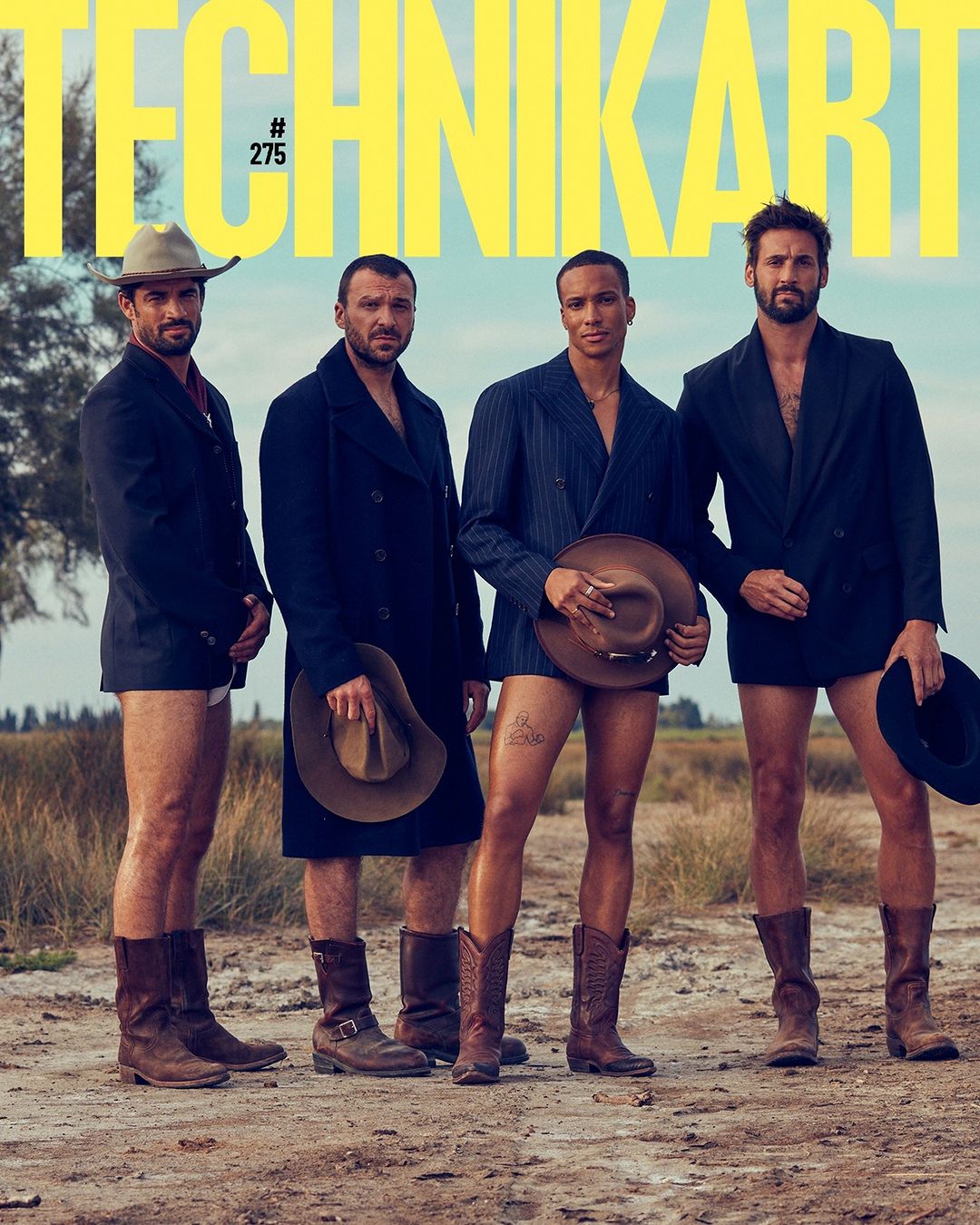 Group of four men in suit jackets and cowboy boots posing in an arid landscape, showcasing fashion and outdoor style on a magazine cover.