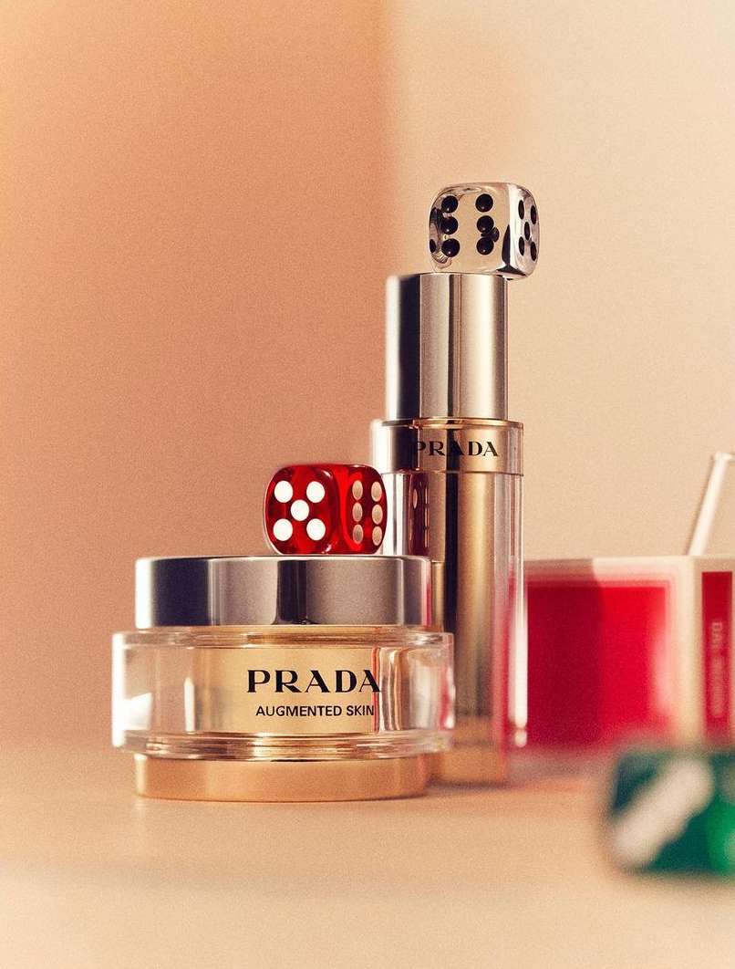 Prada cream jar and serum bottle still life with red and clear dice stacked on the bottles, product shot on peach background.