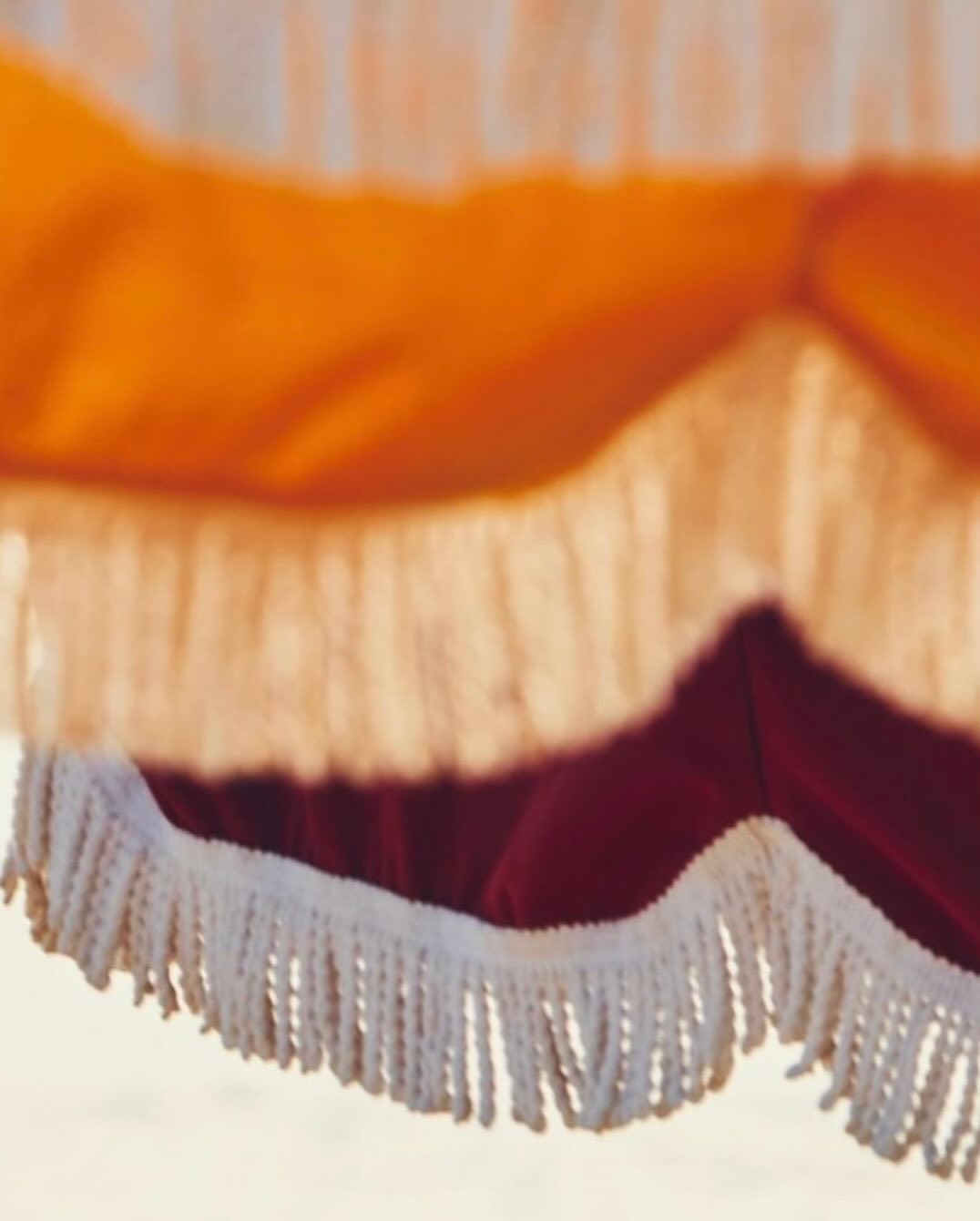 Close-up of a colorful beach umbrella with white fringe on a sunny day, creating a soft, blurred, abstract, vacation mood.