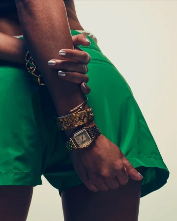 Close-up portrait of a person wearing green shorts and gold jewelry including a wristwatch and bracelets by photographer Romin Favre.