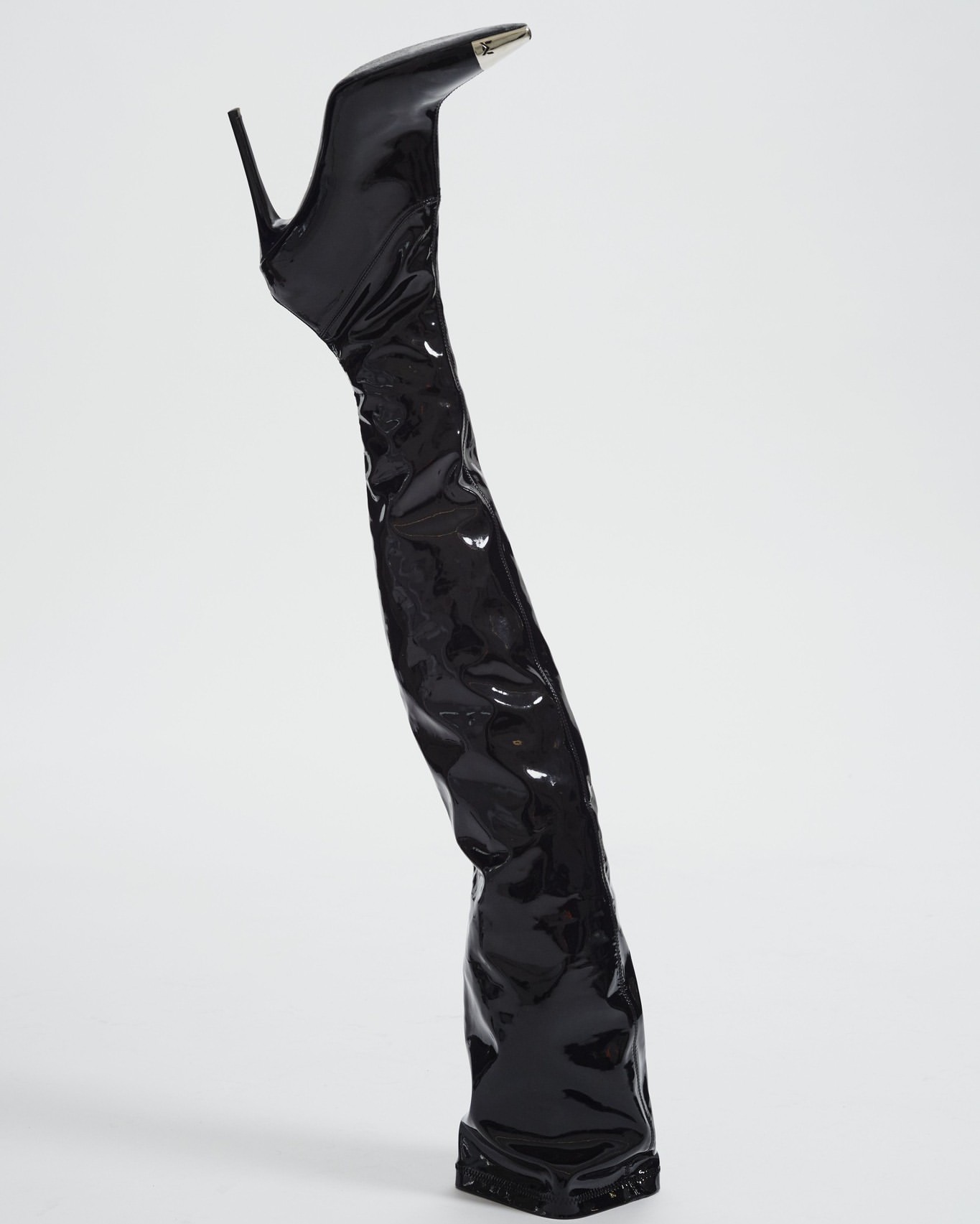 Elevated view of a single, shiny black stiletto-heeled thigh high boot with a silver tip on a white seamless background.