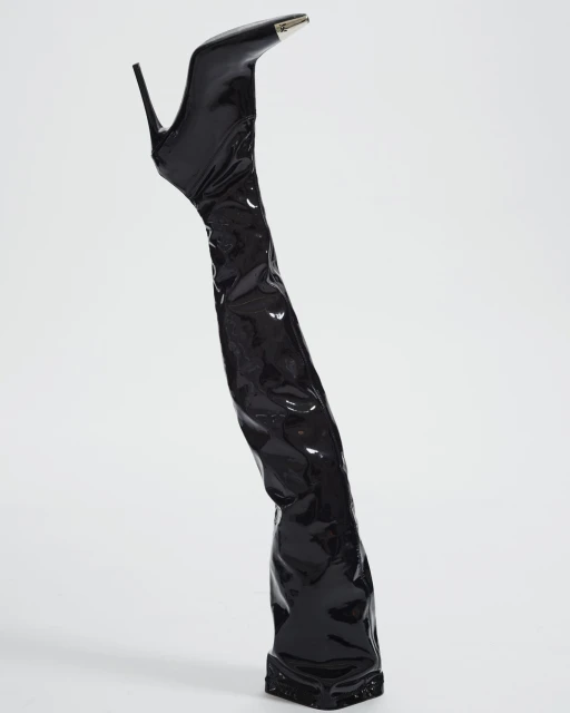 Elevated view of a single, shiny black stiletto-heeled thigh high boot with a silver tip on a white seamless background.