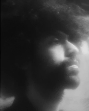Monochrome portrait of a man with a beard looking upwards in a dimly lit setting, featuring soft lighting and blurry aesthetic.
