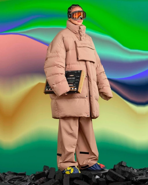 Full-length shot of a woman wearing ski goggles and oversized puffy coat with loose pants, holding a synthesizer on abstract background.