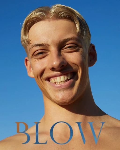 Close-up portrait of a smiling young adult male with blond hair against a clear blue sky, with 'BLOW' text overlay at the bottom.