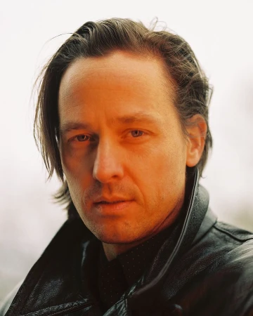 Close-up portrait of a man in his 40s wearing a black leather jacket with warm lighting on his face.