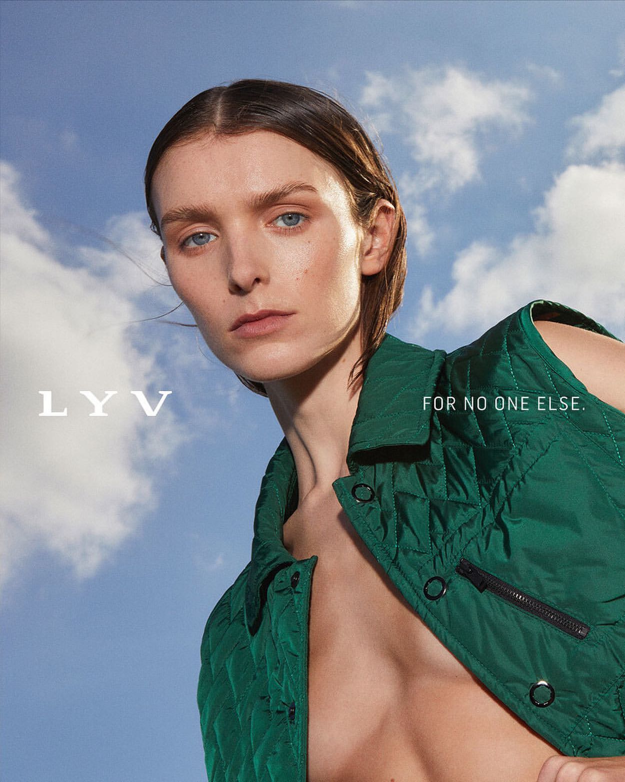 Fashion portrait of a woman with neutral expression, wearing a green vest, against a blue sky with clouds, fashion, beauty, outdoor.