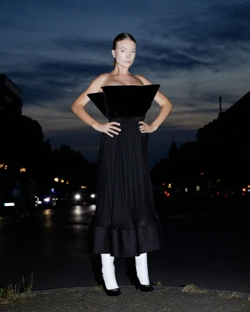 Woman in a structured black strapless dress and white tights standing outdoors at night on a street.
