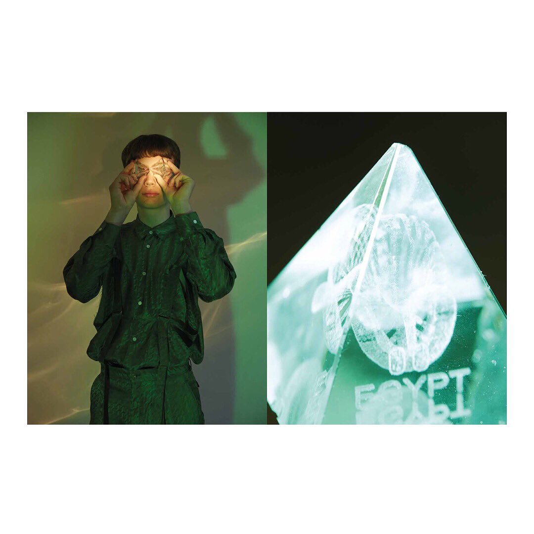 Adult with patterned shirt and pyramid-shaped object with text 'Egypt'. Green color palette with soft lighting and artistic composition.