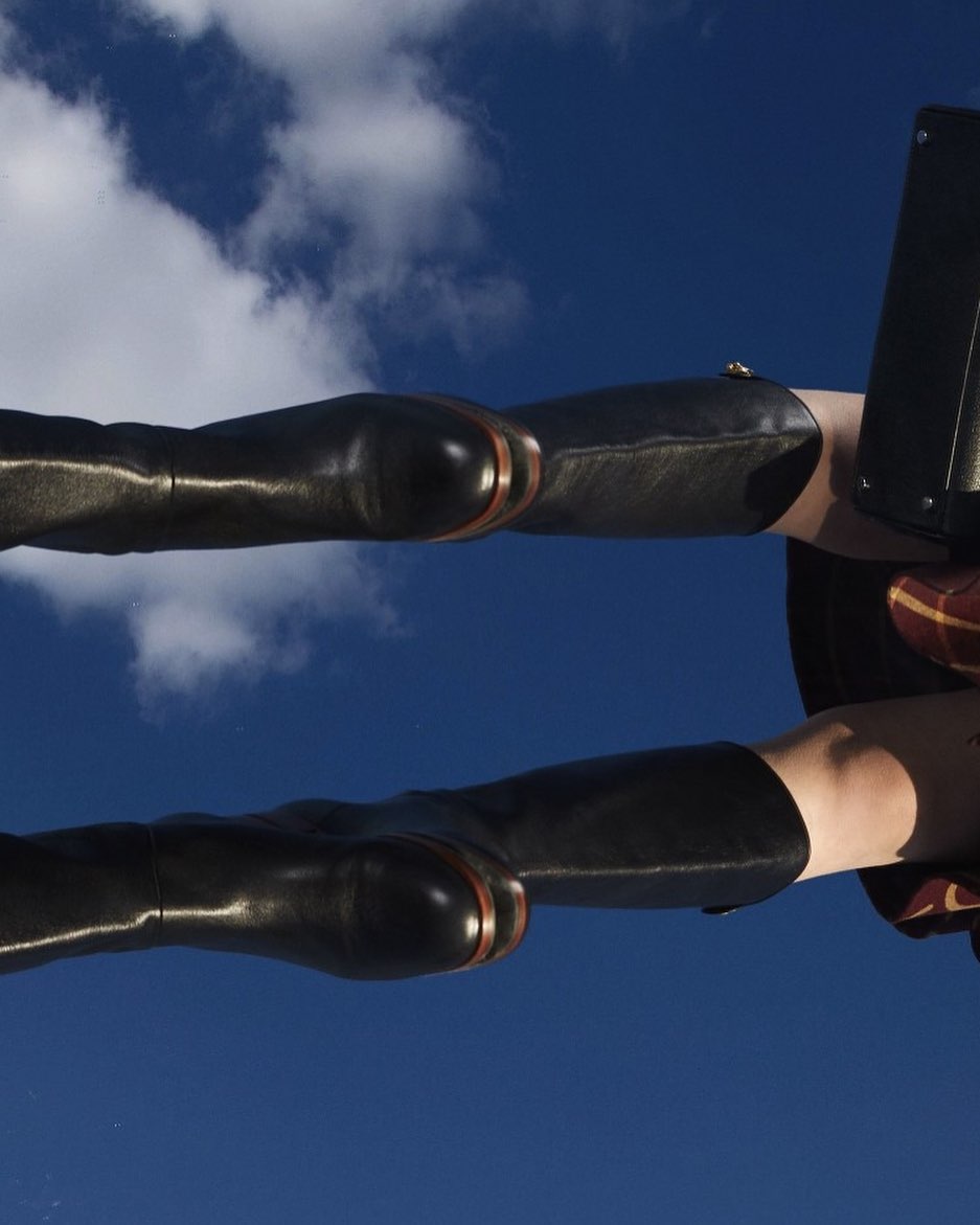 Fashion shot showcasing two pairs of black leather thigh-high boots against a blue sky with clouds; legs angled, creating symmetry.