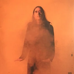 Portrait of a man with long hair in a black garment against an orange background with wispy smoke or vapor obscuring the lower half
