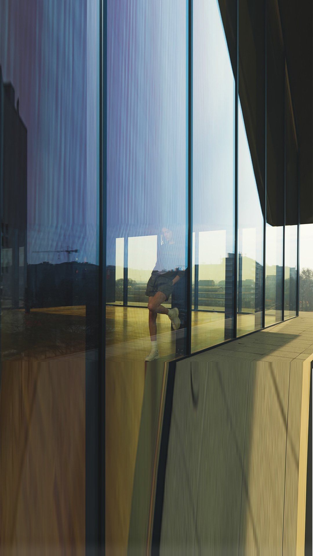 Adult is reflected in building's glass exterior with the city buildings in the background, in an urban setting, during daytime.