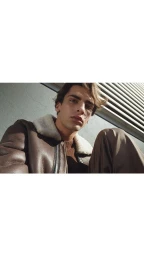 Young man in a brown shearling jacket with a white collar outdoors in natural sunlight directed by Rosamaria Montalbano