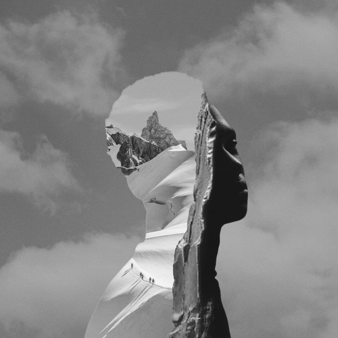 Black and white artistic shot of mountain climbers visible within a face silhouette, set against a cloudy sky and snowy mountain range.