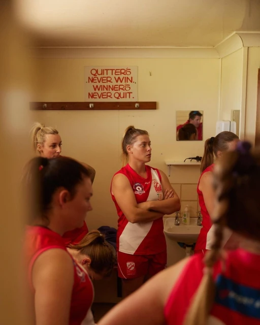 Female athletes in team jerseys gather in an indoor locker room with a motivational quote on the wall. Sports and teamwork.
