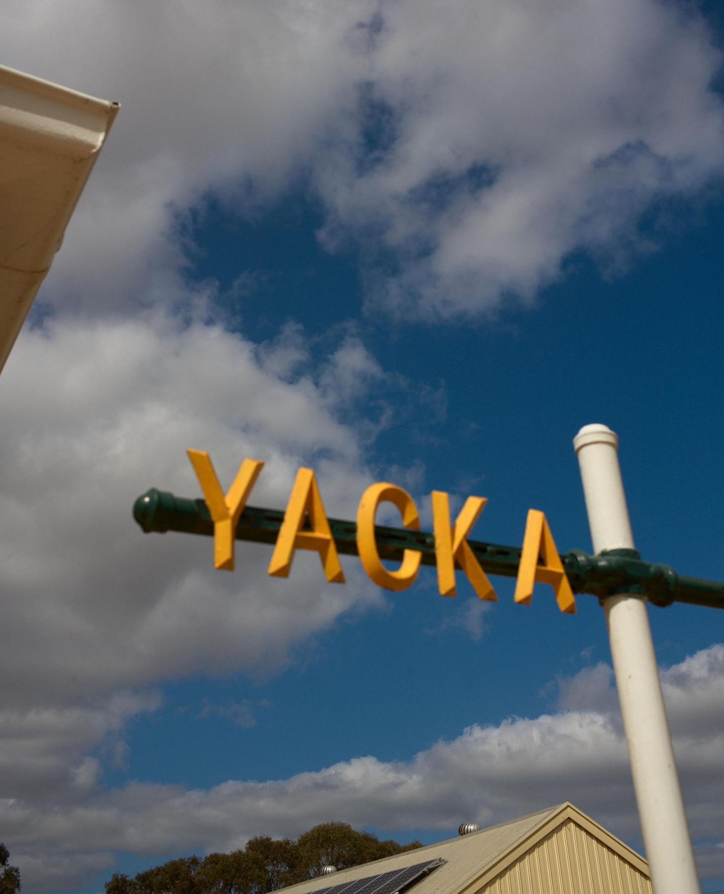 Yellow YACKA sign on a green pole against a blue sky with white clouds, photographed by Cory White.
