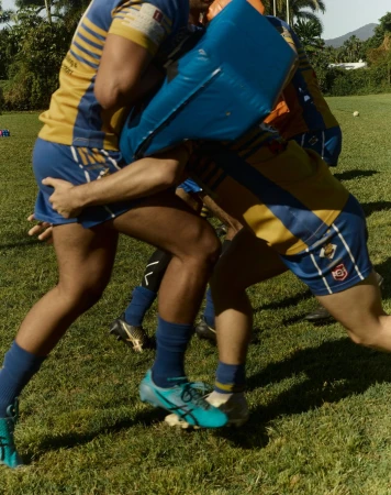 Rugby players practicing a tackle drill on a grassy field, photographed by Cory White.