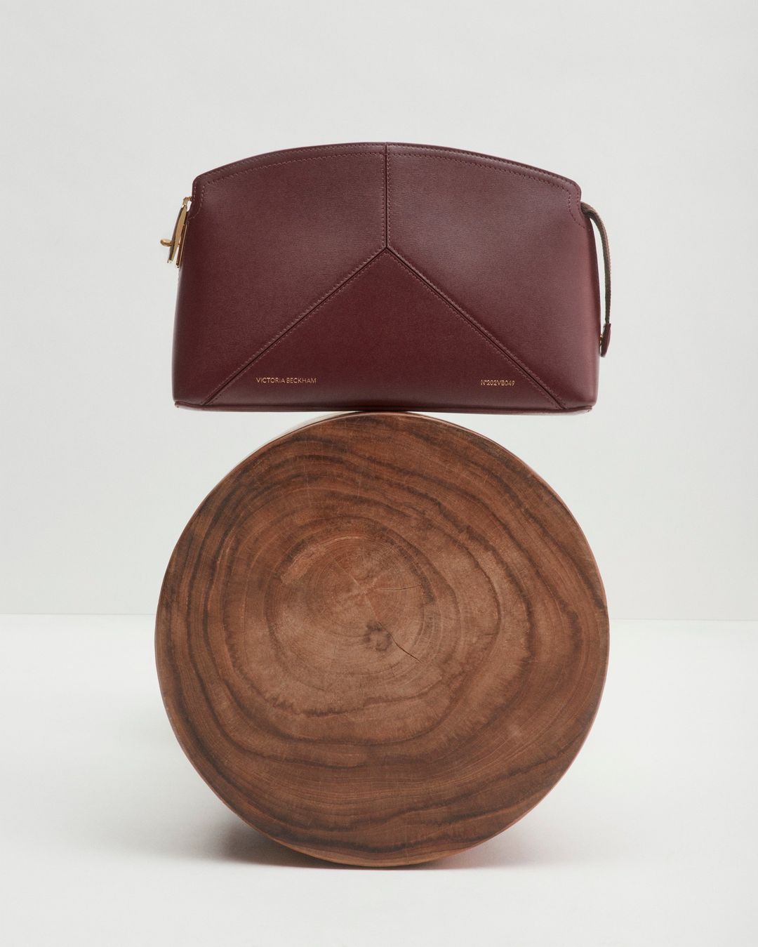 Burgundy leather handbag on a wooden stand against a plain white background in a studio-style product shot. Minimalist aesthetic.